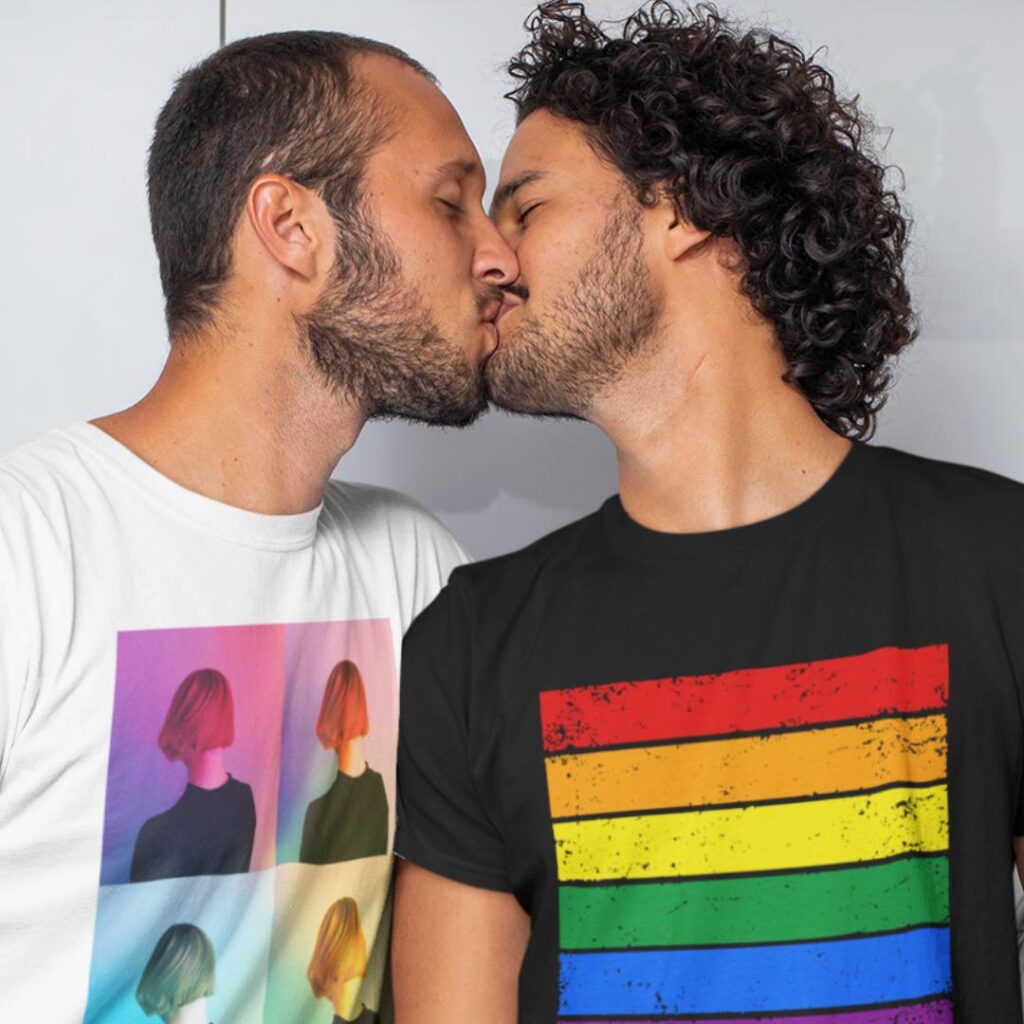 Foto de dois homens se beijando, um deles usando uma camiseta da PrideTag Shop com as cores do arco-íris da bandeira do orgulho LGBT+