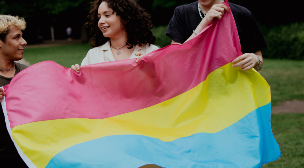 Grupo de três pessoas LGBT segurando uma bandeira do orgulho pansexual.